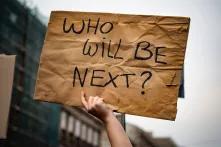 a hand holding up a "who will be next?" sign at a protest in Budapest