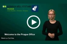 Logo of the Heinrich Böll Stiftung Prague (top left), woman gesturing in International Sign Language, Play button