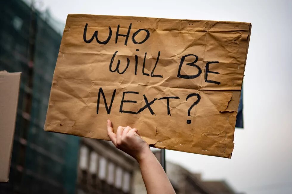 a hand holding up a "who will be next?" sign at a protest in Budapest