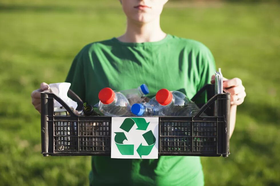 Osoba drží bedýnku s plastovými lahvemi a znakem recyklace