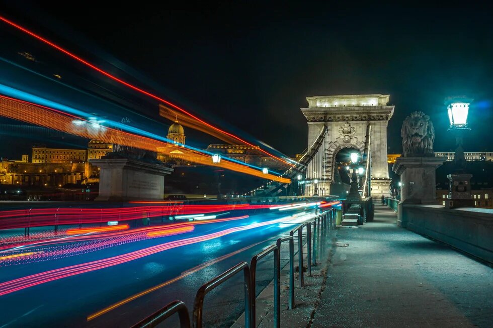 Long-exposure night photograph of Budapest's Chain Bridge with colorful light trails from passing traffic,